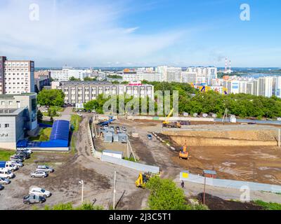 Kemerovo, Russia - 24 giugno 2021. Paesaggio urbano con edifici residenziali e un cantiere in primo piano, una zona industriale con fumo Foto Stock