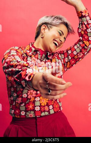 Donna che balla divertendosi. Spensierate la giovane donna che balla e sorride allegramente mentre si alza su uno sfondo rosso. Giovane donna con capelli tinti sentire Foto Stock