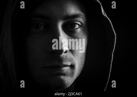 Primo piano ritratto in bianco e nero di un giovane uomo con un cappuccio sulla testa che guarda grumpy in un'atmosfera buia Foto Stock