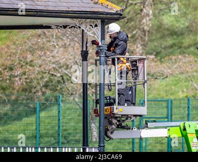 Workman on Cherry Picker with safety harness painting band stand metallwork in Warminster, Wiltshire, UK il 7 aprile 2022 Foto Stock