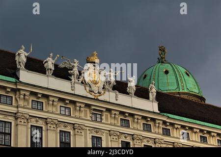 Guardando le sculture sul tetto del Palazzo Imperiale di Hofburg con la cupola di Hofburg sullo sfondo come si vede dalla piazza interna del Castello. Foto Stock
