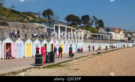 Persone passeggiando oltre tradizionali capanne vittoriane spiaggia costeggiando il lungomare a Lyme Regis in una soleggiata giornata di primavera nel Dorset resort Regno Unito Foto Stock