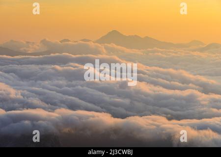 Vista mozzafiato del drone di folte nuvole bianche che galleggiano contro le cime di montagna e cielo arancione alba al mattino nella natura Foto Stock