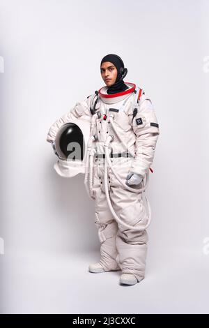 Corpo pieno di astronauta maschio colombiano in spacesuit con casco in mano in piedi in studio su sfondo bianco e guardando la macchina fotografica Foto Stock