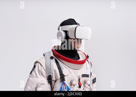 Cosmonaut maschile colombiano in uniforme che interagisce con il cosmo virtuale in occhiali in studio su sfondo bianco Foto Stock