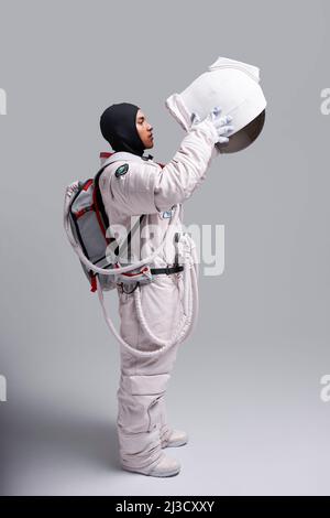 Vista laterale dell'astronauta in spacesuit togliendo casco protettivo con visiera in studio su sfondo bianco Foto Stock