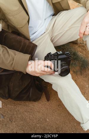 Dall'alto, uomo irriconoscibile in abiti casual con fotocamera seduta su terreno asciutto e ammirare il crinale di montagna durante il viaggio in campagna Foto Stock