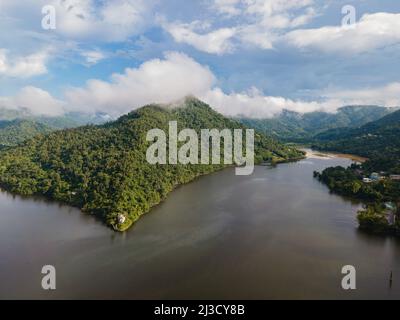 Vista sul lago tranquillo e tortuoso che scorre attraverso una valle collinare coperta da fitte foreste e nuvole Foto Stock