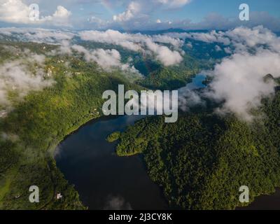 Vista sul lago tranquillo e tortuoso che scorre attraverso una valle collinare coperta da fitte foreste e nuvole Foto Stock