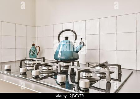 bollitore in metallo blu posto su stufa a gas in cucina con pareti piastrellate bianche in appartamento Foto Stock