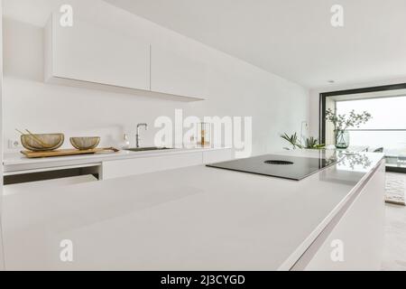Cucina interna con piano cottura con ventilatore incorporato posto su un'isola cucina vicino ad un piano di lavoro con lavello e utensili da cucina Foto Stock