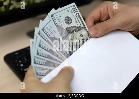 Busta con dollari USA in mani maschili. L'uomo tira i soldi da una busta sullo sfondo della tastiera del PC, sui salari, sui bonus o sul concetto di tangente Foto Stock