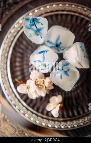 Fiori surgelati per la cura del corpo su vassoio d'argento vintage concetto di pelle fresca. Composizione creativa con petali blu congelati in cubetti di ghiaccio e melo blos Foto Stock