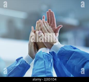 Cooperazione per un'operazione riuscita. Scatto corto di una squadra di chirurghi che si danno a vicenda un alto cinque. Foto Stock