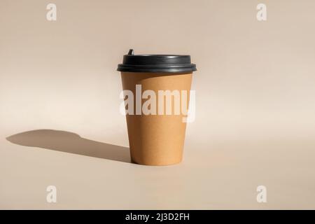 Una tazza di carta da caffè marrone. Mock-up con coperchio. Set di tazze di carta artigianale per caffè o tè su sfondo beige. Tazze riciclate monouso Foto Stock