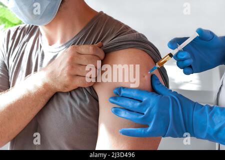 Mani del medico che inietta il vaccino del coronavirus covid-19 in siringa di vaccino al muscolo del braccio dell'uomo caucasico per l'immunizzazione del covid. Foto Stock