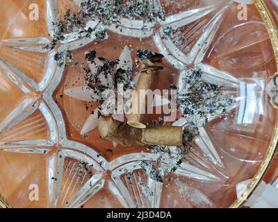 Due sigari affumicati si trovano sulle ceneri in un posacenere sfaccettato di cristallo da vicino Foto Stock