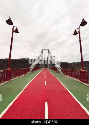 Strada asfaltata di colore rosso sul ponte in prospettiva. Lampioni sui lati Foto Stock