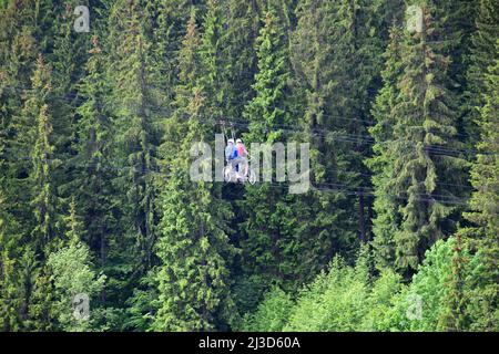 Il giovane uomo e la donna cavalcano speciali biciclette, scivolando su corde alte sopra il terreno sullo sfondo di una foresta verde Foto Stock