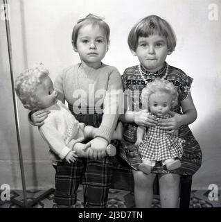 1961, storica, due bambine che sting per una foto che tiene le loro bambole, Stockport, Manchester, Inghilterra, Regno Unito. Foto Stock