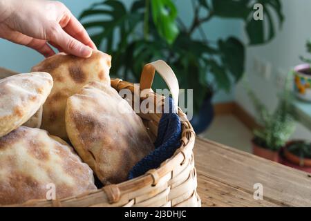 Le mani della donna collocano il pane della pita fatto in casa in un cestino di legno sul vecchio tavolo di legno. Spazio di copia. Foto Stock