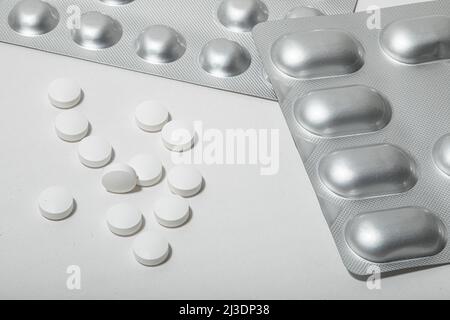 primo piano della confezione blister della compressa di alluminio e alcune pillole bianche sciolte su uno sfondo bianco nessuno persone Foto Stock