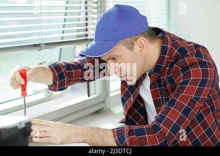 man avvita un cacciavite nella parete di legno Foto Stock