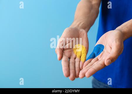 Uomo con cuore disegnato nei colori della bandiera Ucraina sulle sue palme su sfondo blu Foto Stock