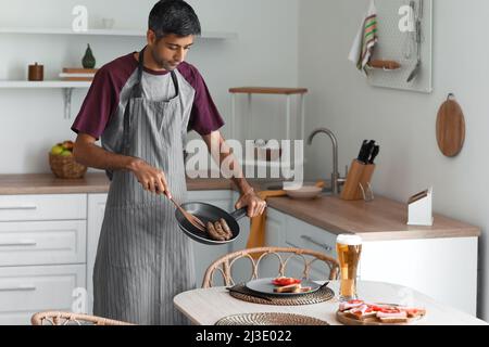 Bell'uomo che mette le salsicce fritte sul piatto in cucina Foto Stock