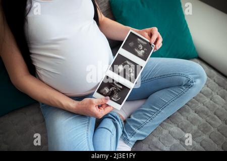 Una donna incinta mostra il suo rapporto ecografico e il suo feto. Tiene le immagini del bambino di ultrasuono con entrambe le sue mani davanti al suo pancino grande. Foto Stock