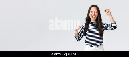 Stile di vita, emozioni della gente e concetto casuale. Entusiasta donna asiatica felice partecipare alla competizione sportiva, cannonaggio e cannonaggio per la squadra, alzando le mani su e. Foto Stock