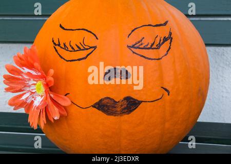 Faccia femminile disegnata su zucca arancione decorata con fiore ad Halloween. Foto Stock