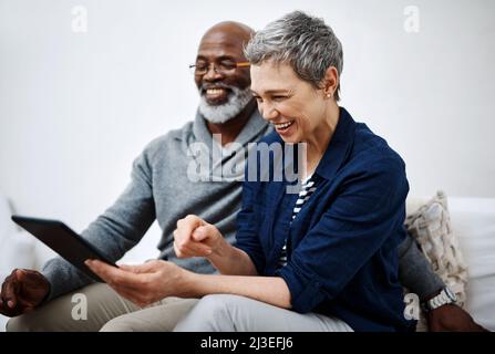 Shes ha sempre qualcosa di divertente per mostrarmelo. Scatto di una coppia anziana affettuosa usando un tablet mentre si rilassa sul divano a casa. Foto Stock