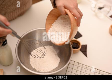 Cuoco femminile versare una tazza di farina in un recipiente di miscelazione, preparando i biscotti ingredienti in cucina. Biscotti di cottura concetto. Foto Stock