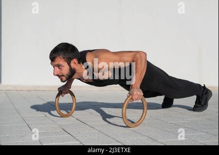 Un uomo in abbigliamento sportivo nero che fa il push-up anello all'aperto. Foto Stock