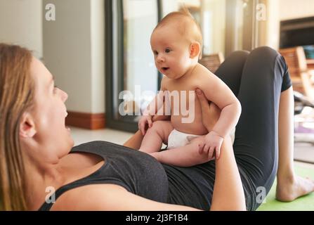 Immagino che lo Yoga la aiuti a farmi ridere. Scatto di una giovane madre e del suo bambino a casa. Foto Stock