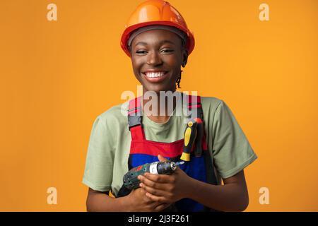 Sorridente giovane afroamericana in hardhat tenendo utensile cacciavite in studio Foto Stock