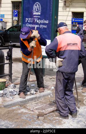 Operai che riparano strade acciottolate, centro città, Lviv, Ucraina Foto Stock