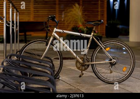 La mountain bike vecchia e sporca è utilizzata per i pendolari parcheggiati nel portabiciclette del centro città. Foto scattata di sera, scarsa luce proveniente dalla strada Foto Stock