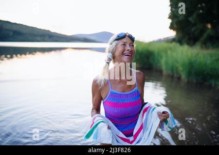 Ritratto di attiva donna anziana nuotatore asciugarsi con asciugamano all'aperto presso il lago. Foto Stock