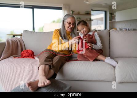 Bambina seduta sul divano con la nonna e imparare a lavorare a maglia in casa. Foto Stock