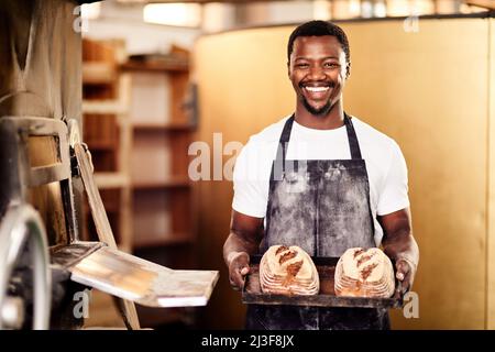 Se volete freschi allora venite alla mia panetteria. Shot corto di un panettiere maschio che tiene in mano il pane appena sfornato nella sua panetteria. Foto Stock