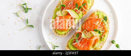Sandwich all'aperto con salmone salato, avocado guacamole e microgreens. Frutti di mare. Cibo sano. Vista dall'alto. Banner. Foto Stock