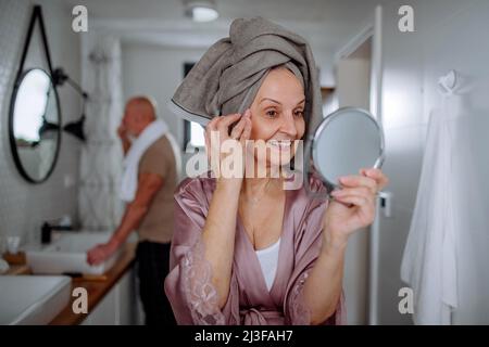 Coppia anziana in bagno, denti spazzolanti e guardando lo specchio, mattina concetto di routine. Foto Stock