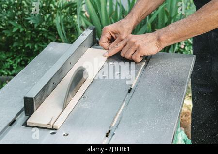 turner lavora su un tornio. Il tavolo di sega. Un uomo ruba un albero con una fresatrice. Un carpentiere esperto taglia un asse di legno con una sega circolare. Foto Stock