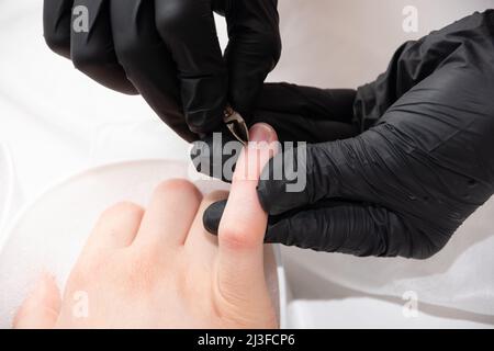 Manicurista che rimuove la cuticola dalle unghie femminili da un pestello di metallo durante l'immersione delle unghie nel bagno al salone delle unghie. Mani durante una cura manicure sessi Foto Stock