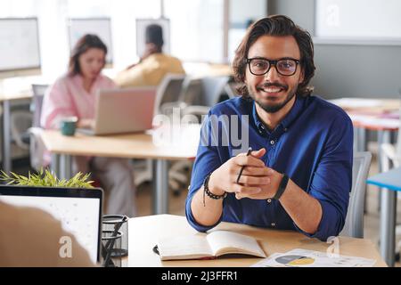 Ritratto di sorridente giovane esperto misto di marketing gara seduta a tavola con pianificatore in ufficio Foto Stock