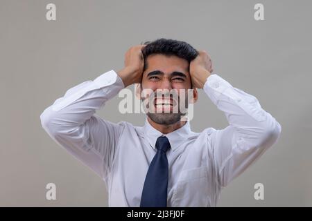 Un giovane arrabbiato in una camicia bianca tirando i capelli con entrambe le mani e gridando Foto Stock