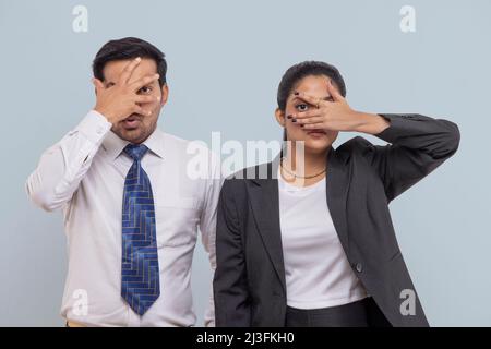 Sorprende la coppia corporativa che copre il viso con le palme e guarda la macchina fotografica attraverso un occhio Foto Stock