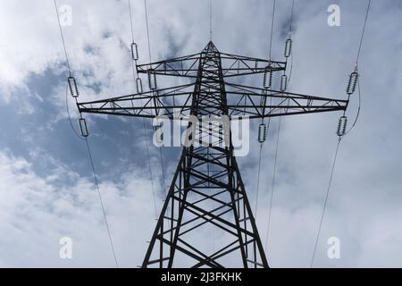 Enorme grande traliccio ad alta tensione visto dal basso con isolatori e linee ad alta tensione contro cielo parzialmente nuvoloso come concetto per l'elettricità e. Foto Stock